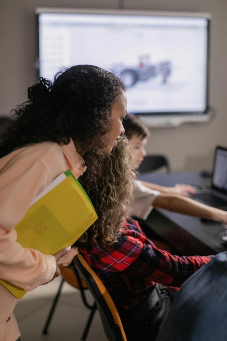 A woman assists students during a computer-based classroom session.